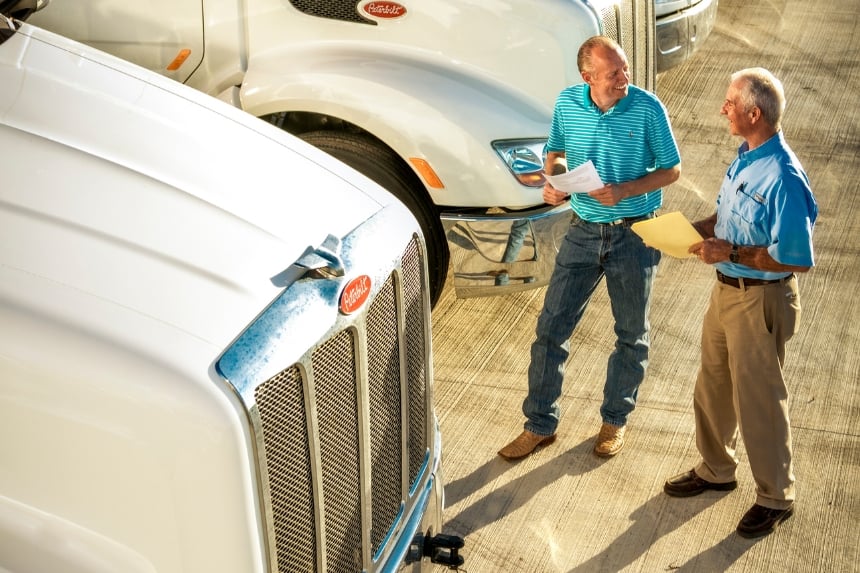 Two men holding papers standing in front of trucks